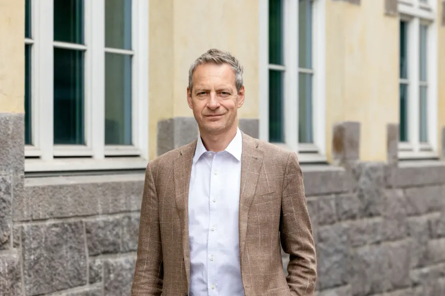 Pressebilde av mann i lys blazer foran bygning