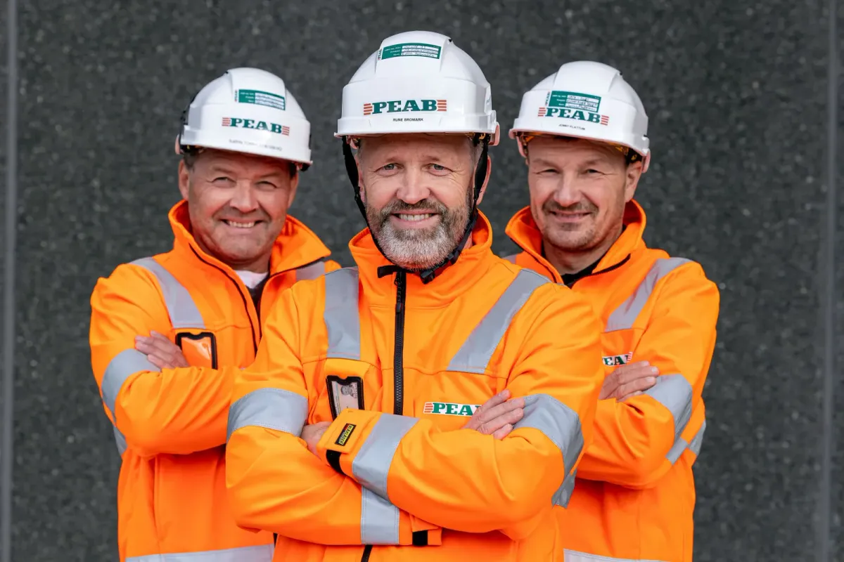 Tre medarbeidere i arbeidstøy og hjelm på arbeidsplassen, bedriftsfoto