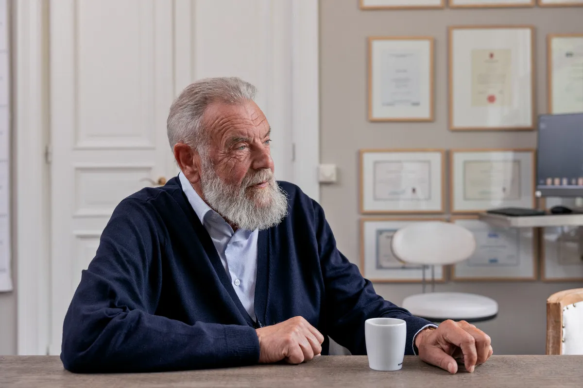 Eldre mann med skjegg ved møtebord med kaffekopp