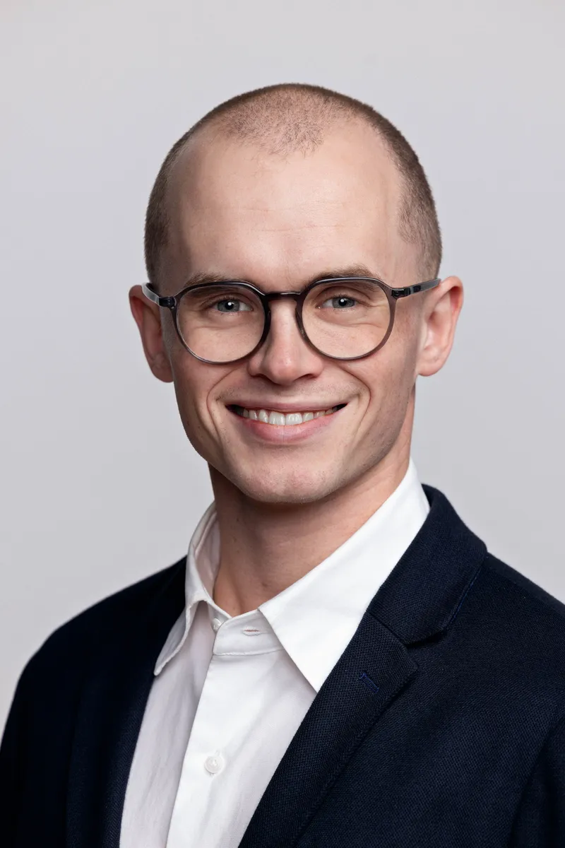 Smilende mannlig leder med briller og blazer, fargeportrett mot grå bakgrunn